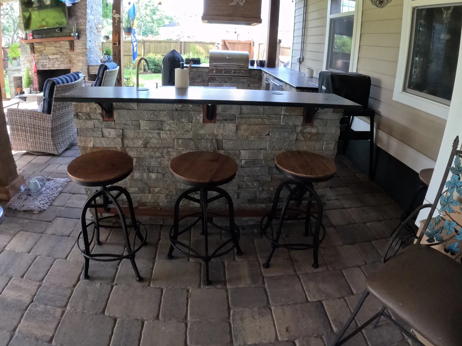 Stone outdoor kitchen bar with a sapele foot rail and bar stools in Summerville, SC Stone outdoor kitchen bar with a sapele foot rail and bar stools in Summerville, SC