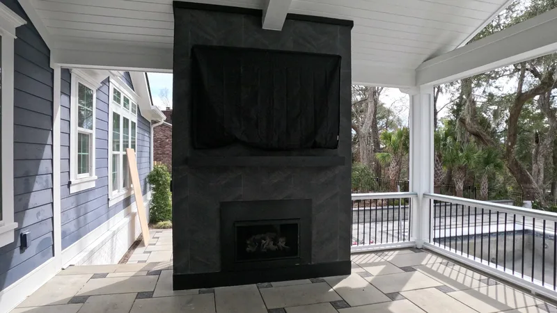 Covered porch fireplace with a dark tile surround and TV in Summerville, SC
