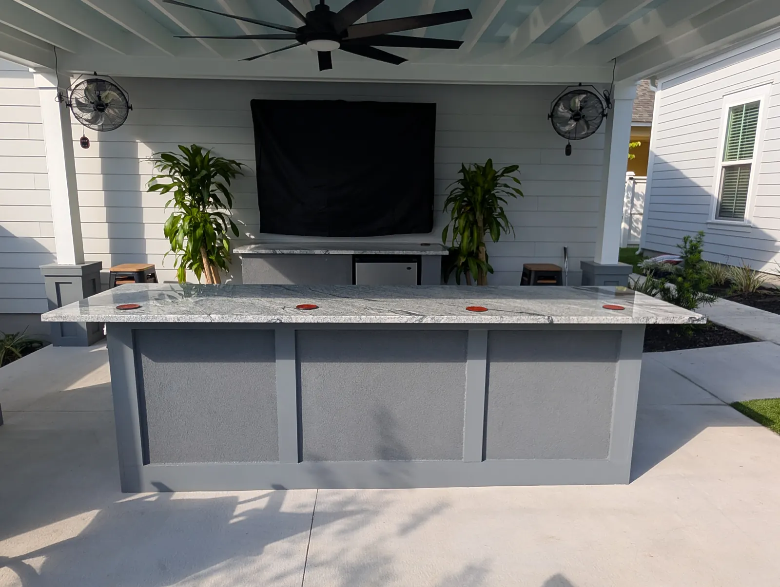 White stucco outdoor kitchen with a granite bar top and mounted TV in Summerville, SC