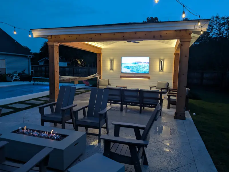 Gas fire table burning beside a lit pool cabana with a mounted TV at night in West Ashley, SC