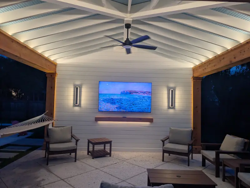 Outdoor living room at night with wall sconces, hidden tape lighting washing the rafter ceiling and a mounted TV in West Ashley, SC