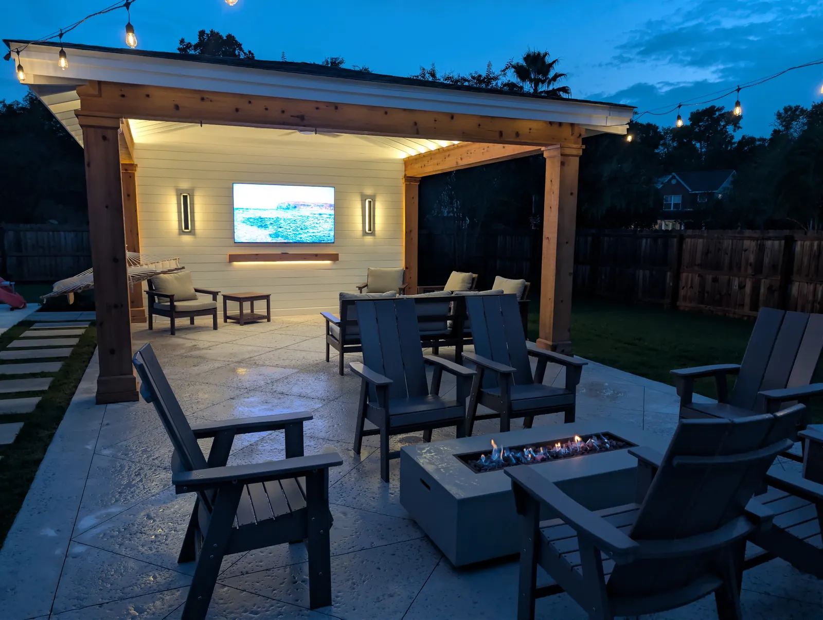 Pool cabana at dusk with a fire table, lounge seating and string lights across the patio in West Ashley, SC Pool cabana at dusk with a fire table, lounge seating and string lights across the patio in West Ashley, SC